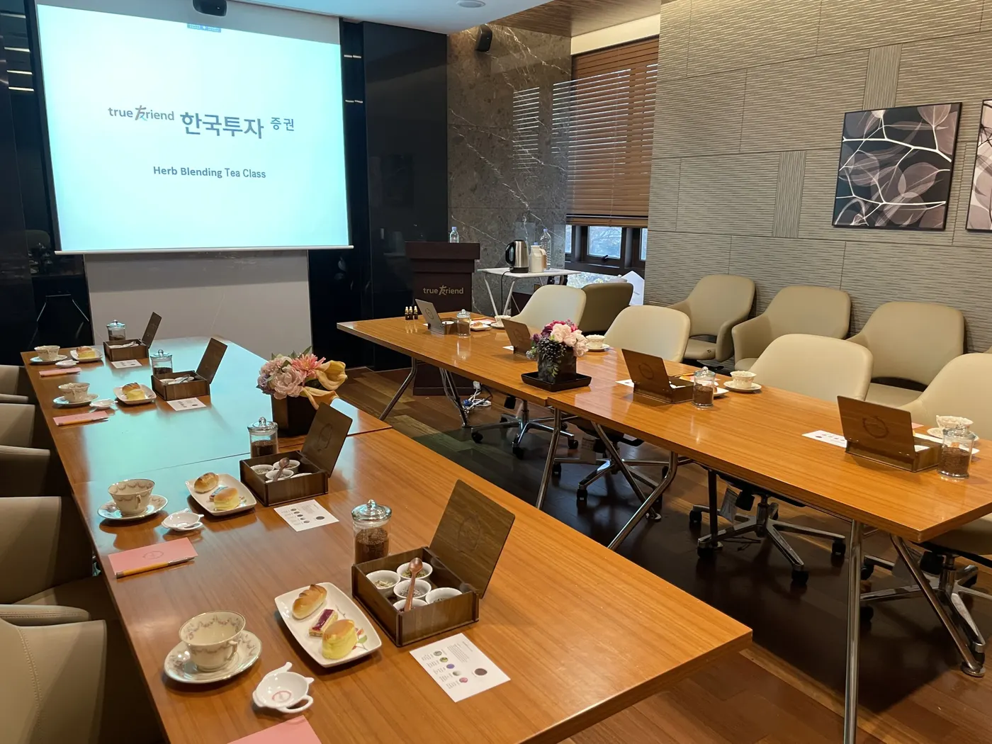 기업힐링교육 프로젝터 화면 앞 긴 테이블에 티와 다과를 세팅한 기업 교육 현장